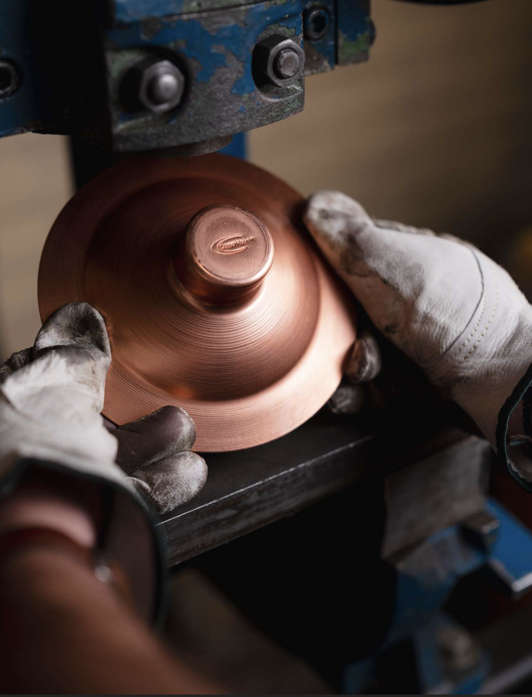 A CopperMoon craftsperson pressing a copper fixture cap on a lathe in the West Point workshop