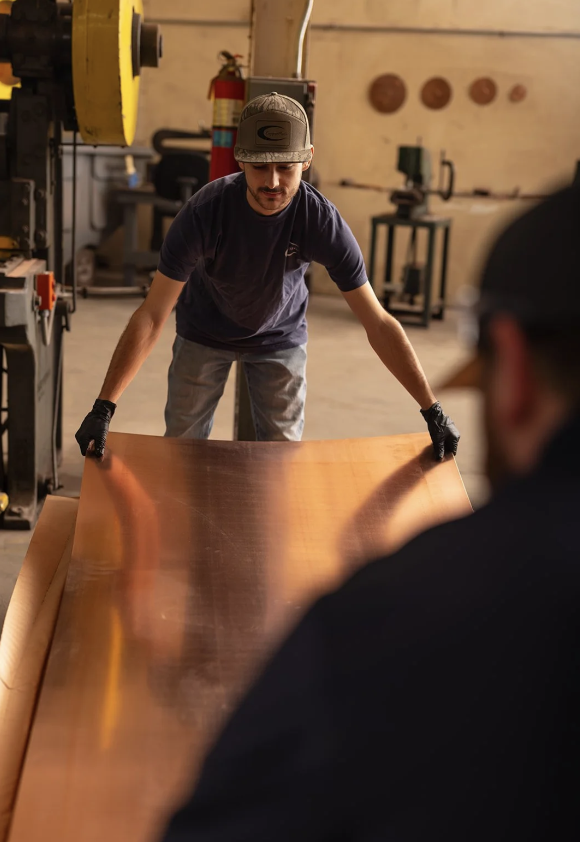 Two CopperMoon workers in the West Point workshop handling a large copper sheet together